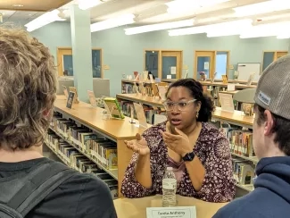 A woman standing at a small round table in a library talking to two students